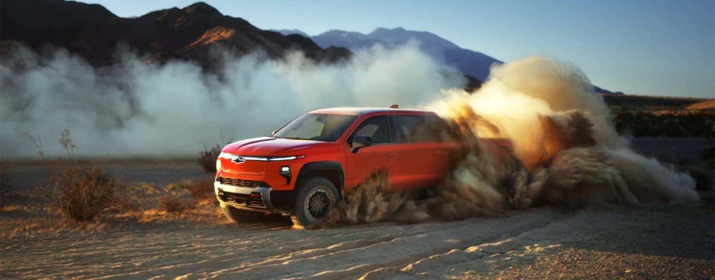 An orange 2026 Chevy Silverado EV for sale near Mint Hill kicking up dust off-road.