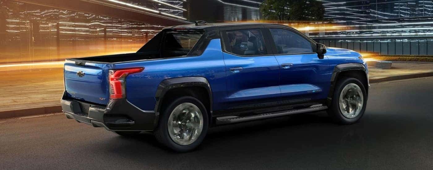 A blue 2024 Chevy Silverado EV driving past buildings.