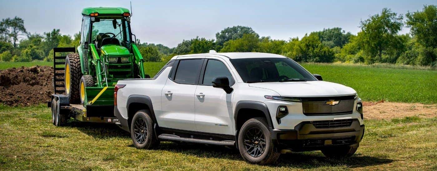 A white 2024 Chevy Silverado EV WT towing a tractor.