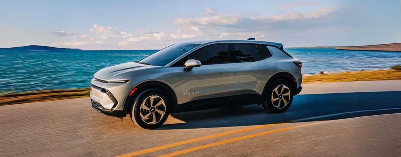 A silver 2025 Chevy Equinox EV for sale near Gastonia driving past a lake.