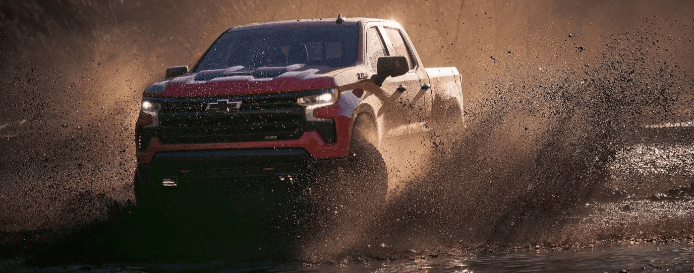 A red 2023 Chevy Silverado 1500 for sale near Concord kicking up mud.