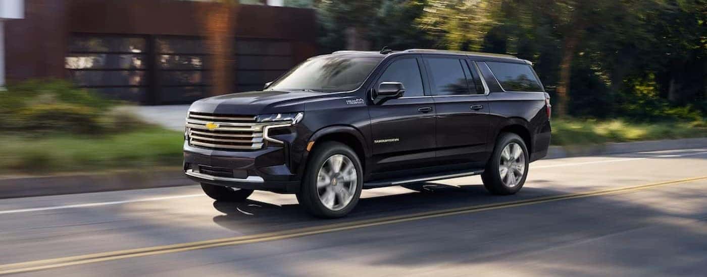 A blue 2023 Chevy Suburban High Country driving to view a used Chevy for sale.