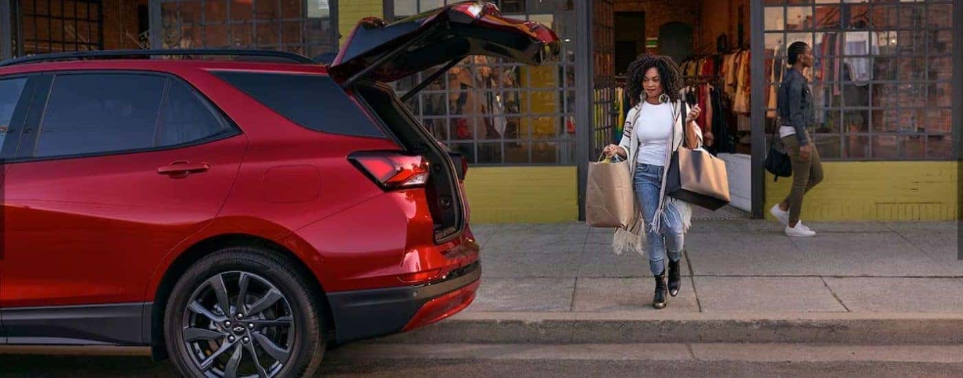 Woman carrying bags to the open hatchback of a red 2024 Chevy Equinox RS.