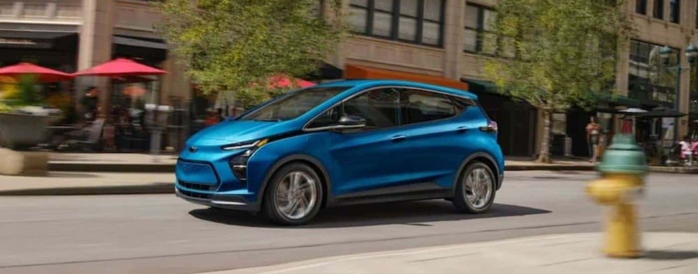 A blue 2023 Chevy Bolt EV driving after viewing a used Chevy for sale in Charlton.