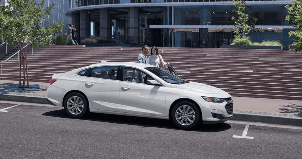 A couple dressed up for a date riding a Chevy Malibu