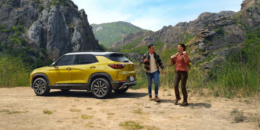 A man and woman beside a yellow Chevy Blazer in a field with mountains behind them.