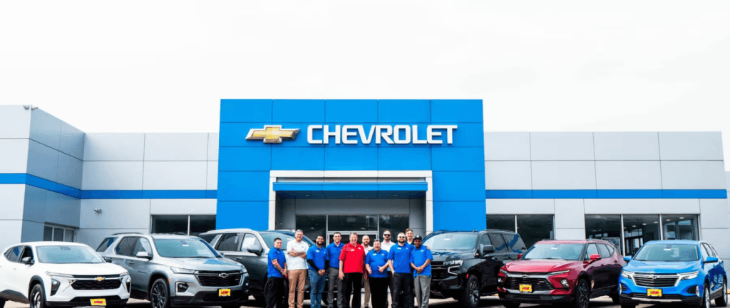 The Richard Lucas team in front of the Chevrolet dealership in New Jersey. Several Chevy cars are parked in front of the store.