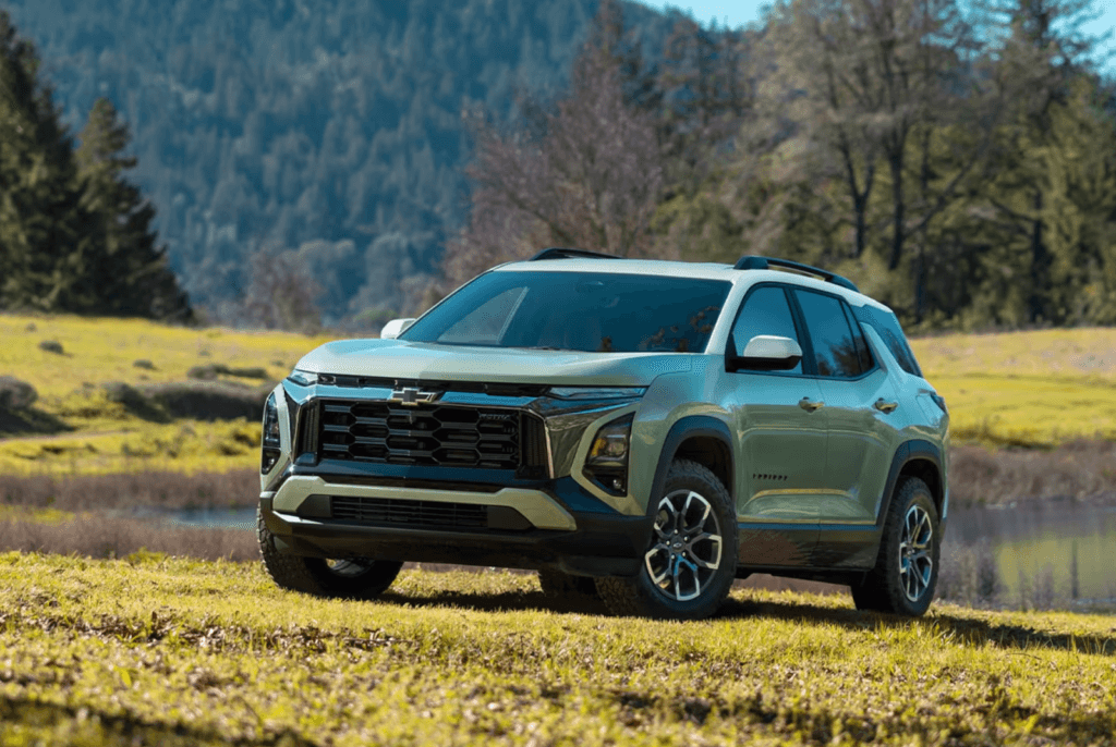  A light green and white Chevy Equniox is parked on a grassy hill in a natural, outdoor setting with trees and a body of water in the background.