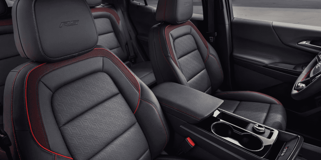 The interior of an SUV showing the front and rear seats upholstered in black leatherette with red stitching and accents. The front headrest has an embossed "RS" logo.