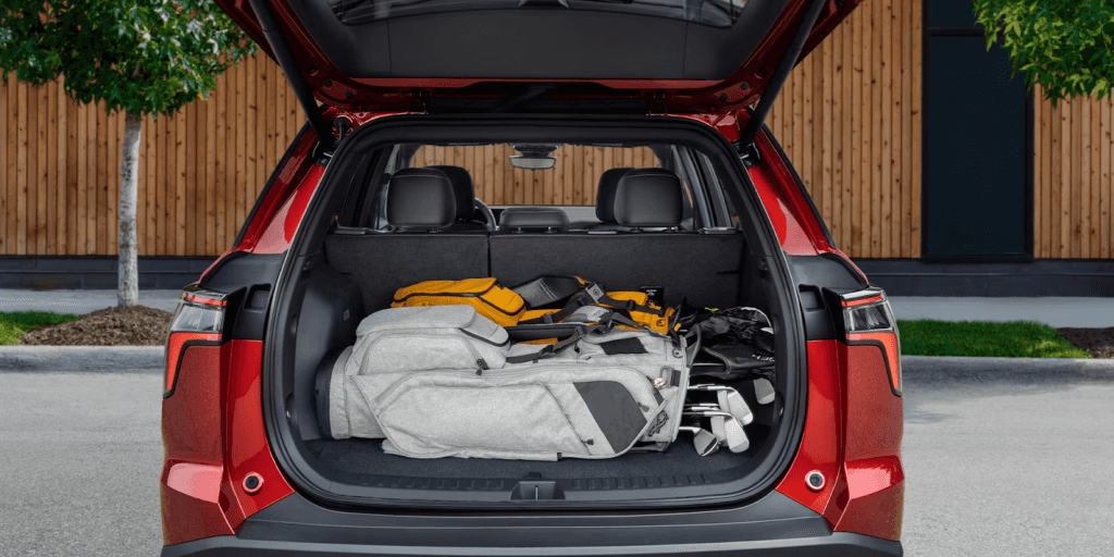 The open rear liftgate of a red SUV, showing the cargo area with the rear seats folded up. The space is storing two golf bags and a yellow and black duffel bag.
