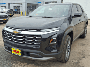A black SUV with a large grille and a chrome accent bar is parked in a car dealership lot. The vehicle has a yellow and red "Lucas" dealer license plate on the front.