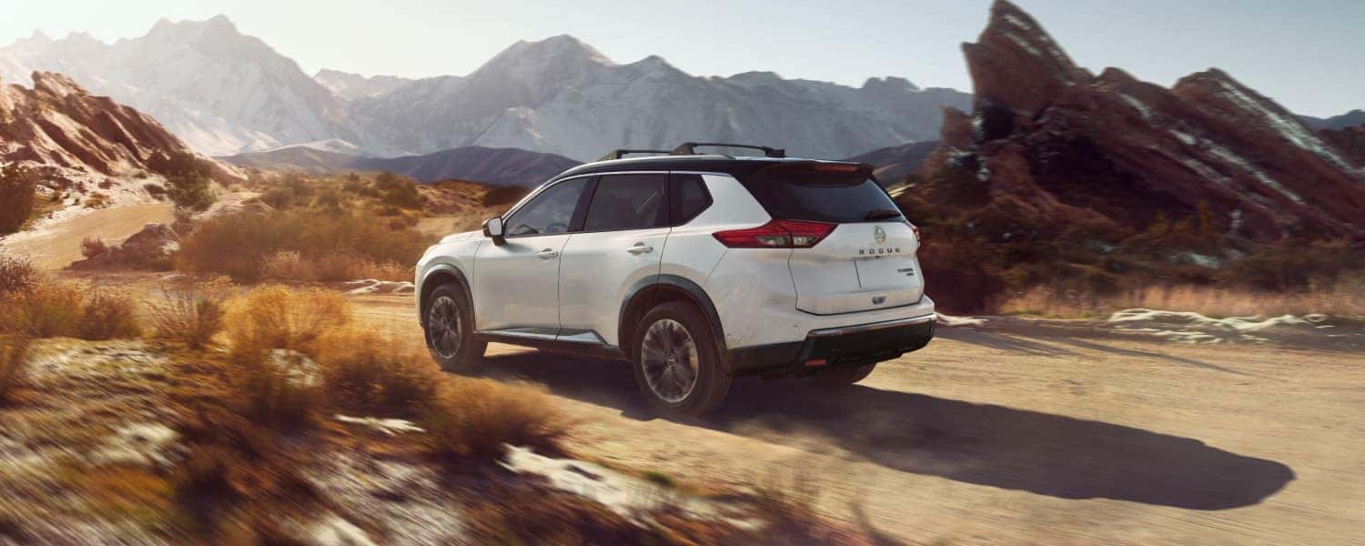 A white 2025 Nissan Rogue driving on a dirt road through a desert.