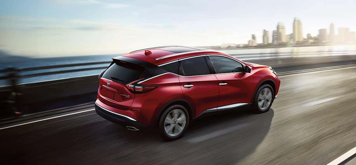 A red 2024 Nissan Murano driving over a bridge towards a city