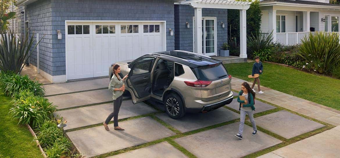 A gray 2024 Nissan Rogue parked in a driveway with the backdoor open and a family around it