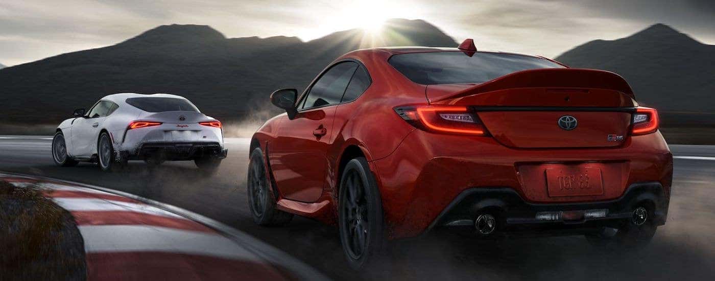 A white 2023 Toyota Supra and a red 2023 Toyota GR86 is shown from the rear at an angle.