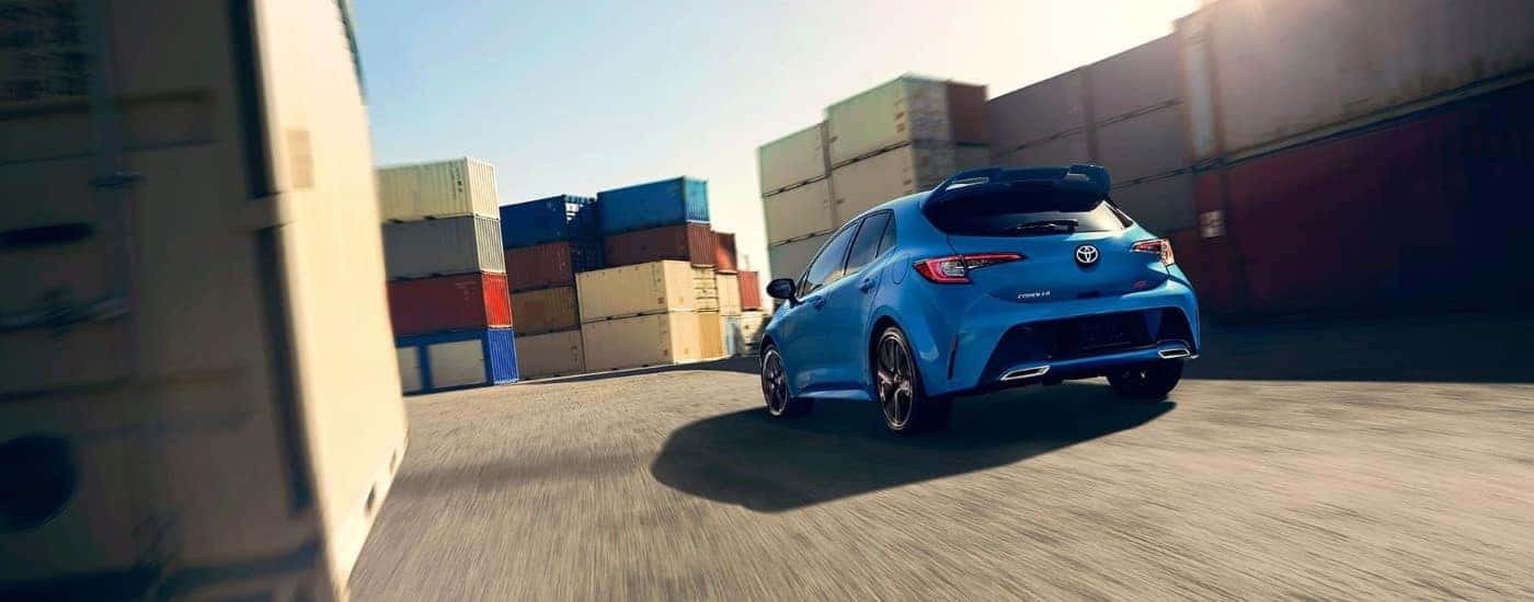 Rear view of a blue 2020 Toyota Corolla XSE driving through stacks of shipping containers.