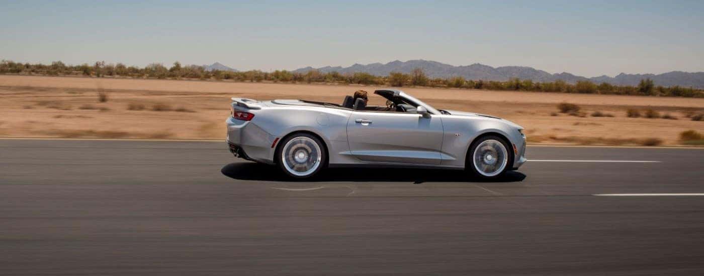 Side view of a silver 2018 Chevy Camaro SS driving with the top down.