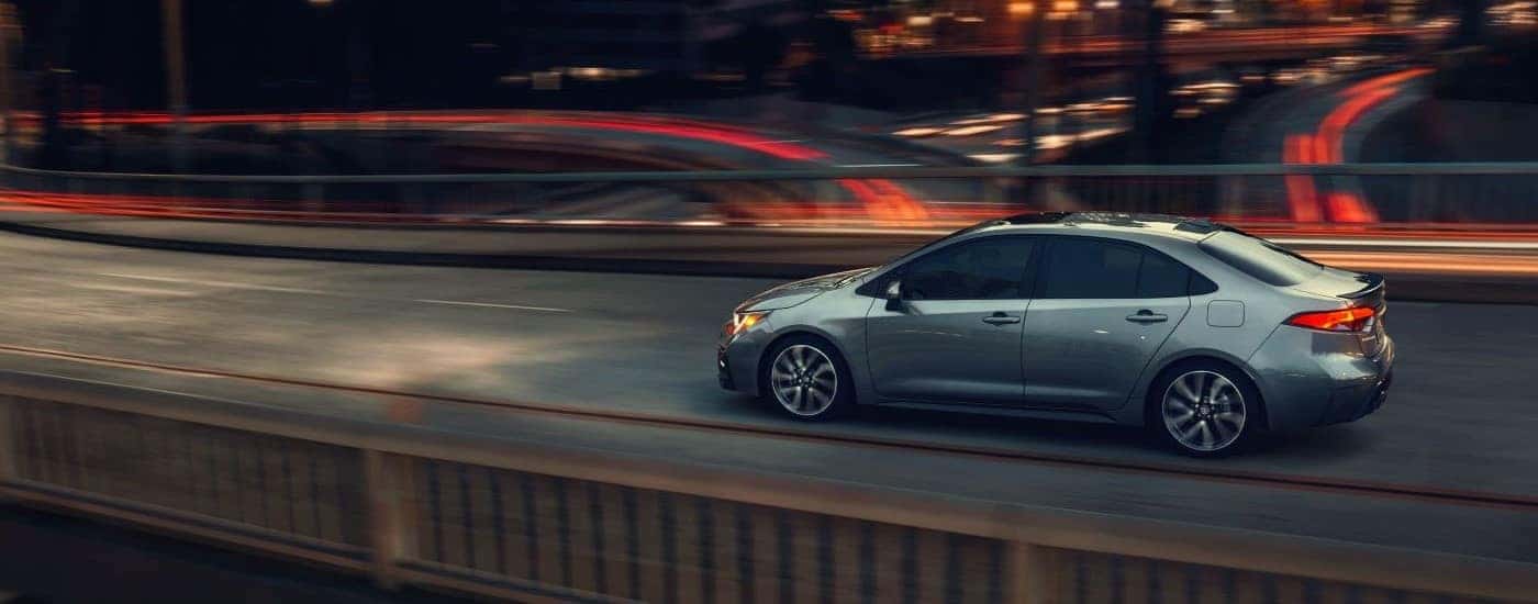Side view of a silver 2021 Toyota Corolla driving over a bridge with blurred lights.