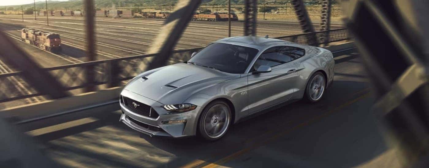 Silver 2023 Ford Mustang GT is shown driving past train tracks.