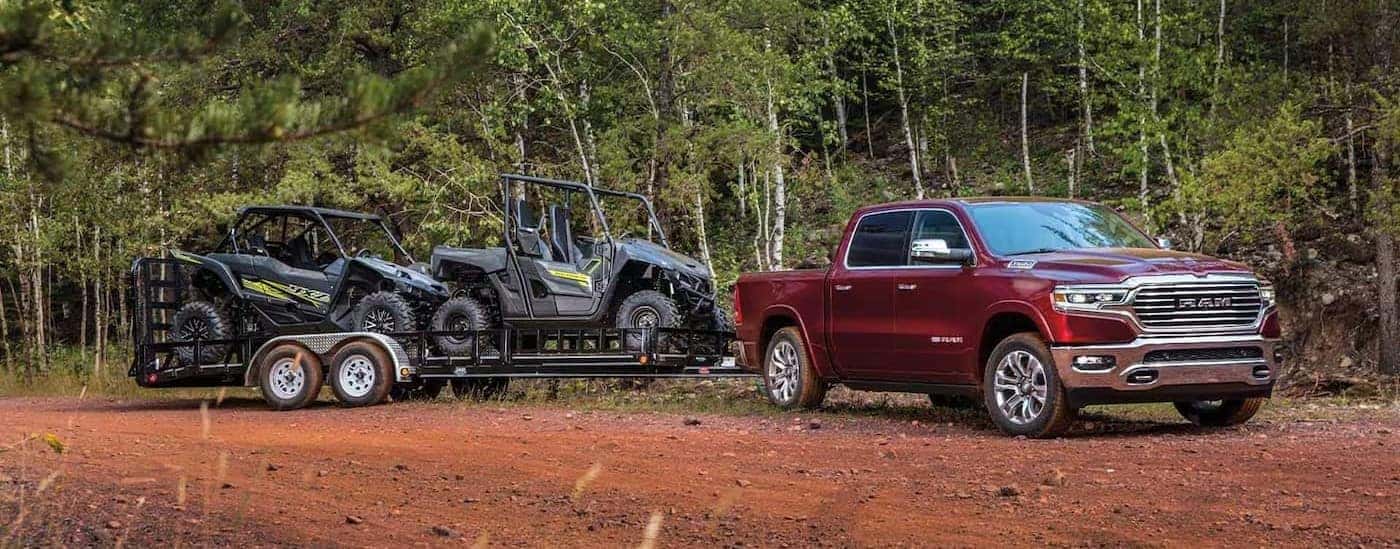 A red 2023 Ram 1500 is shown towing a trailer off-road.