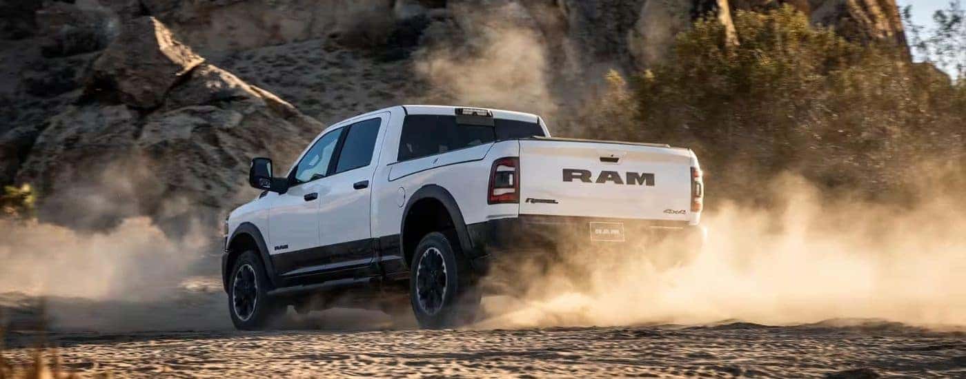 Rear view of a white 2023 Ram 2500 Rebel kicking up dust while off-roading.