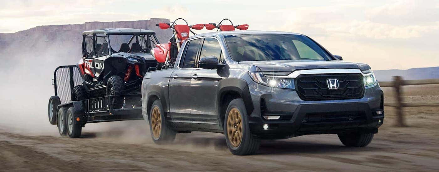 A Silver 2022 Honda Ridgeline RTL-E towing ATVs off-road.