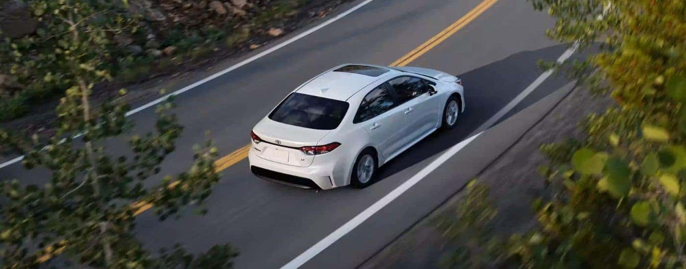 High rear angle view of a white 2023 Toyota Corolla LE driving down a road.