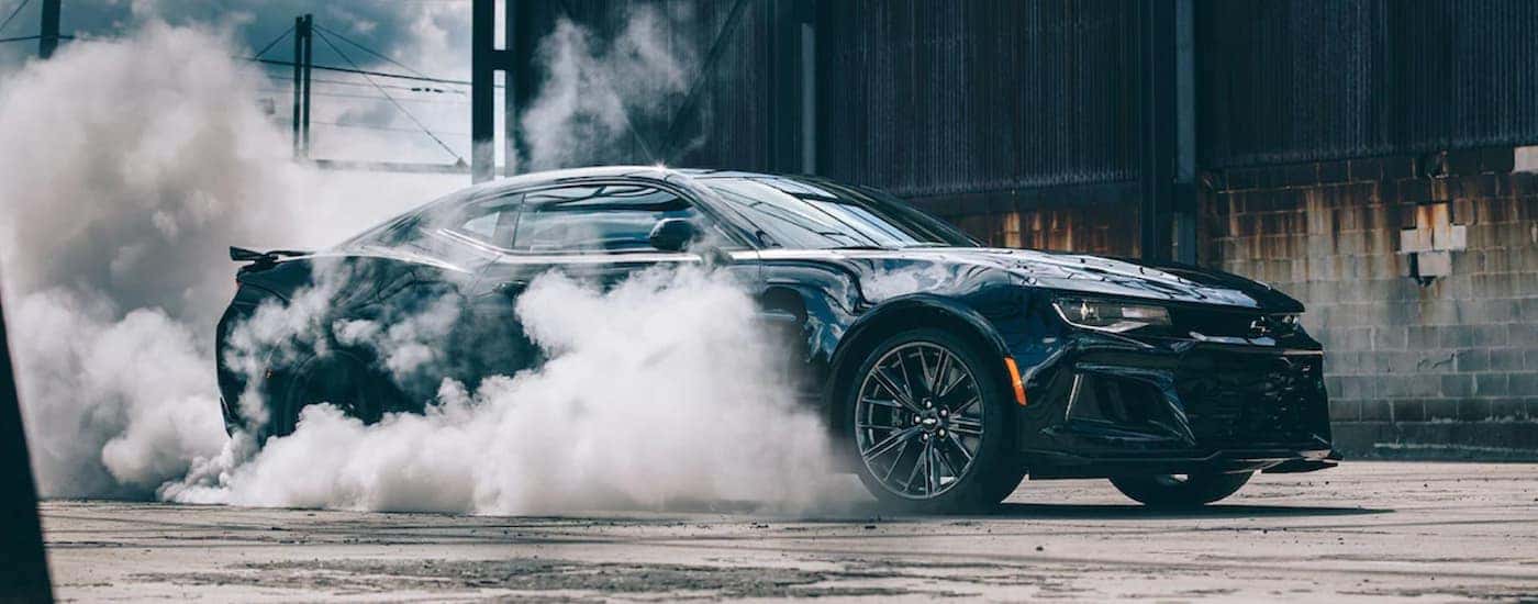 Black 2022 Chevy Camaro performing a burnout near a cement block building