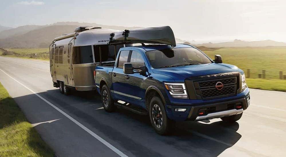 A blue 2024 Nissan Titan is shown towing a trailer on a highway.