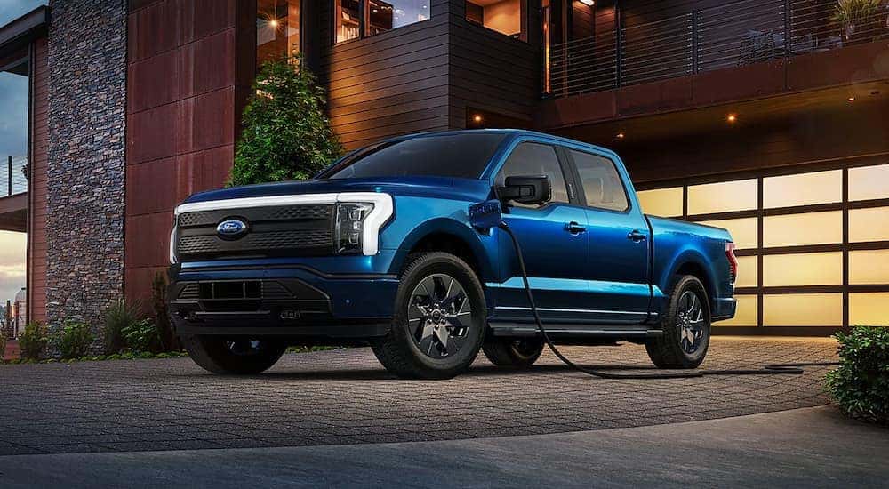 A blue 2022 Ford F-150 Lightning parked on a driveway and charging.