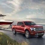 A red 2024 Ford F-150 towing a boat near an ocean.