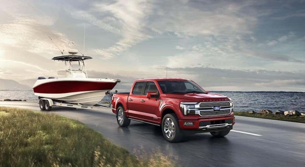A red 2024 Ford F-150 towing a boat near an ocean.