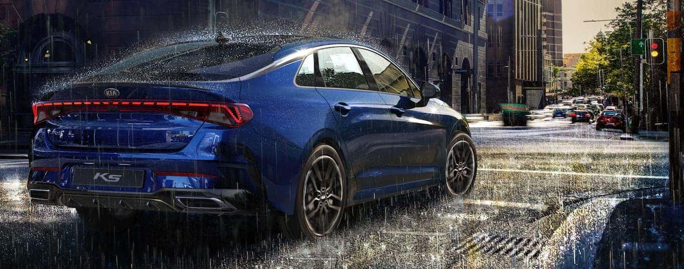 A blue 2025 Kia K5 is shown from the rear at an angle.