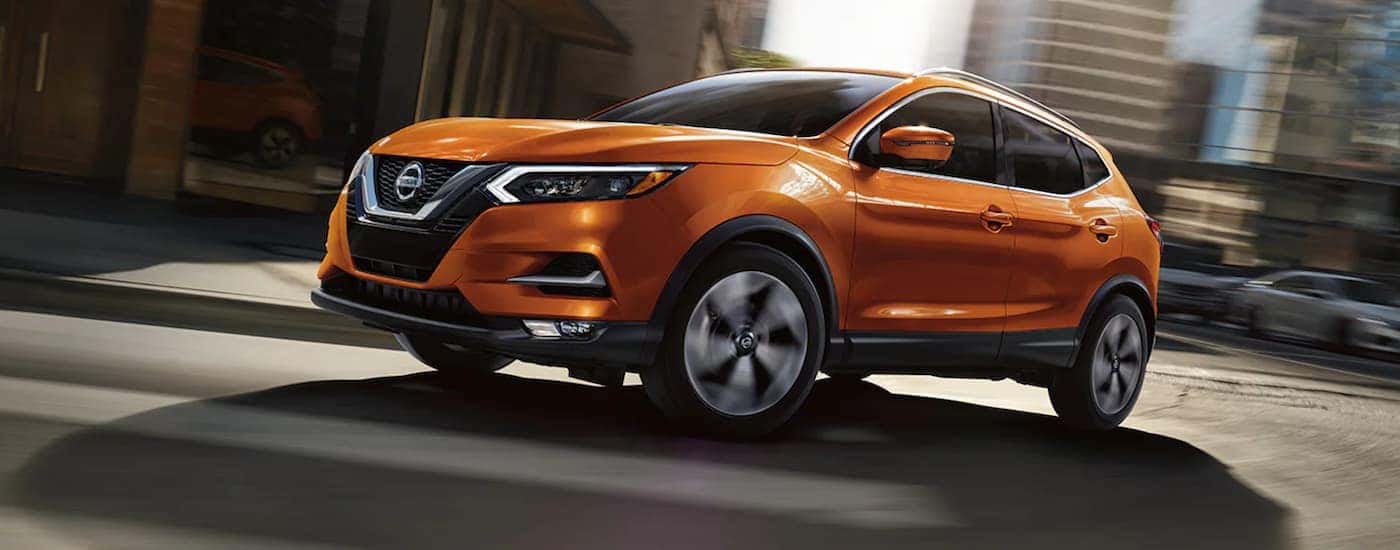 Orange used 2021 Nissan Rogue Sport driving on a city street