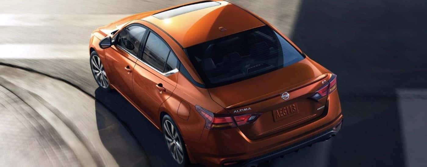 An orange used 2022 Nissan Altima for sale turning on a road