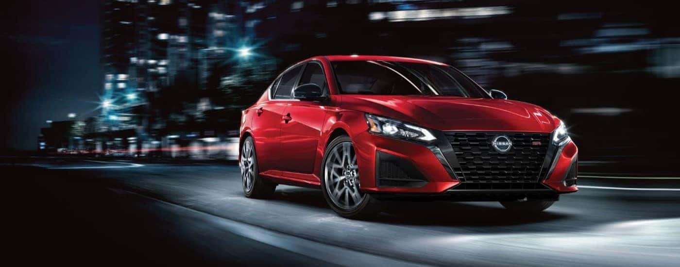 A red used 2023 Nissan Altima SR driving in a city at night