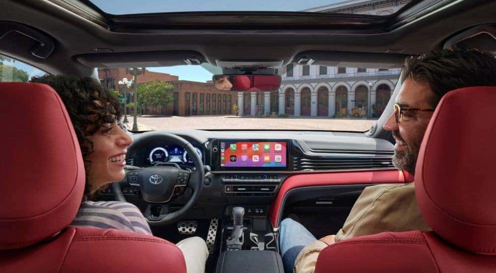 Two people speak in the front seat of a 2025 Toyota Camry with red interior.