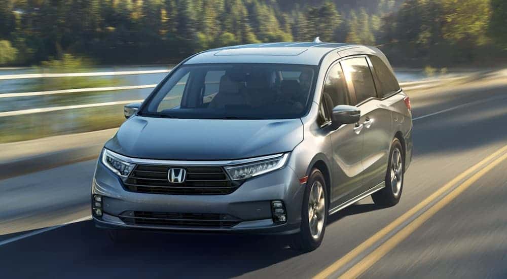 A silver 2023 Honda Odyssey driving to view used vans for sale.