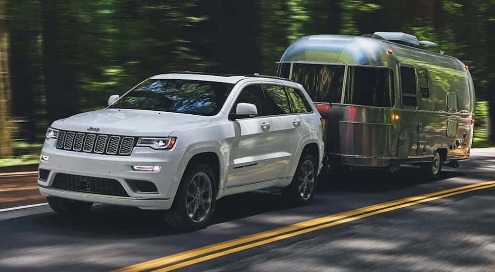 A white 2021 Jeep Grand Cherokee towing a camper