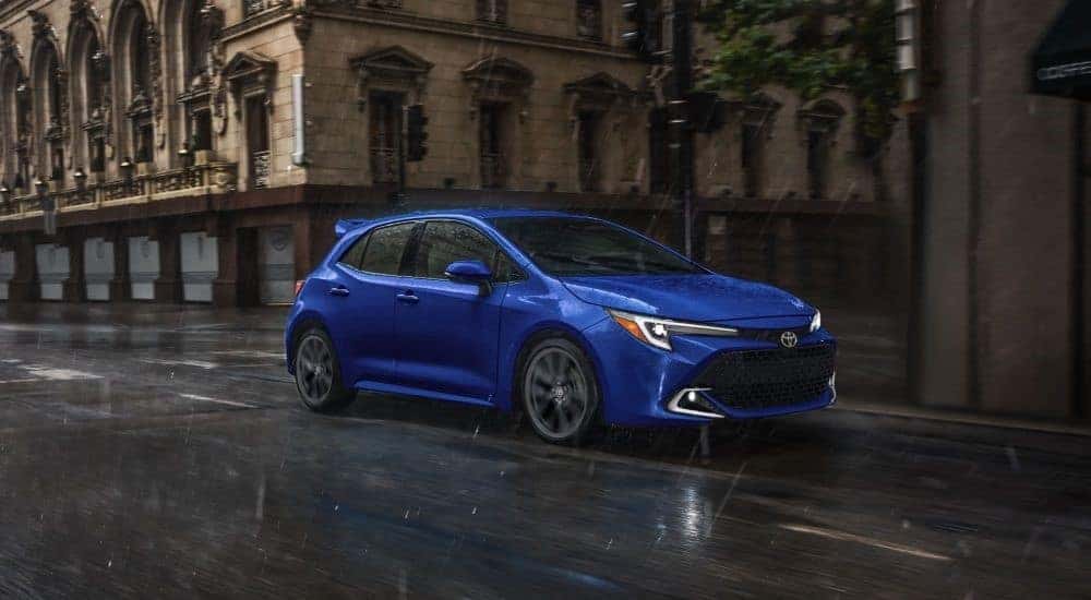 A blue 2024 Toyota Corolla driving on a city street in the rain
