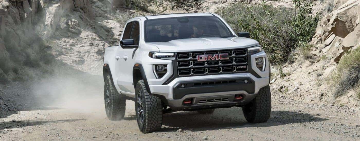 A white 2023 GMC Canyon AT4 driving off-road on a trail