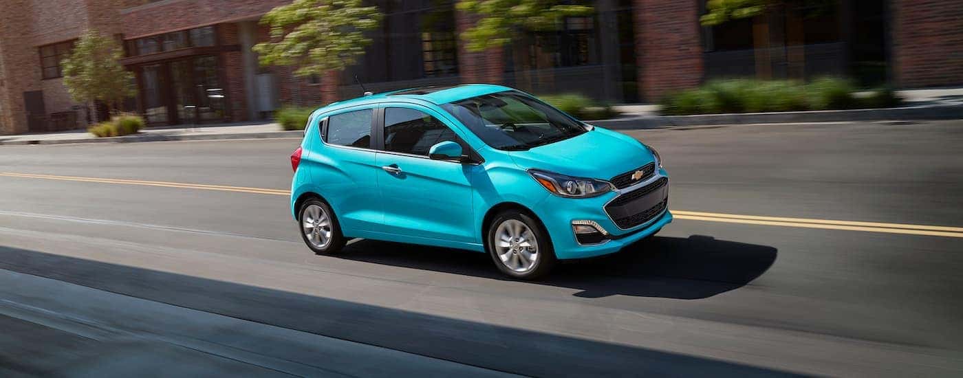 A teal 2021 Chevy Spark is shown driving to visit a used Chevy dealer.