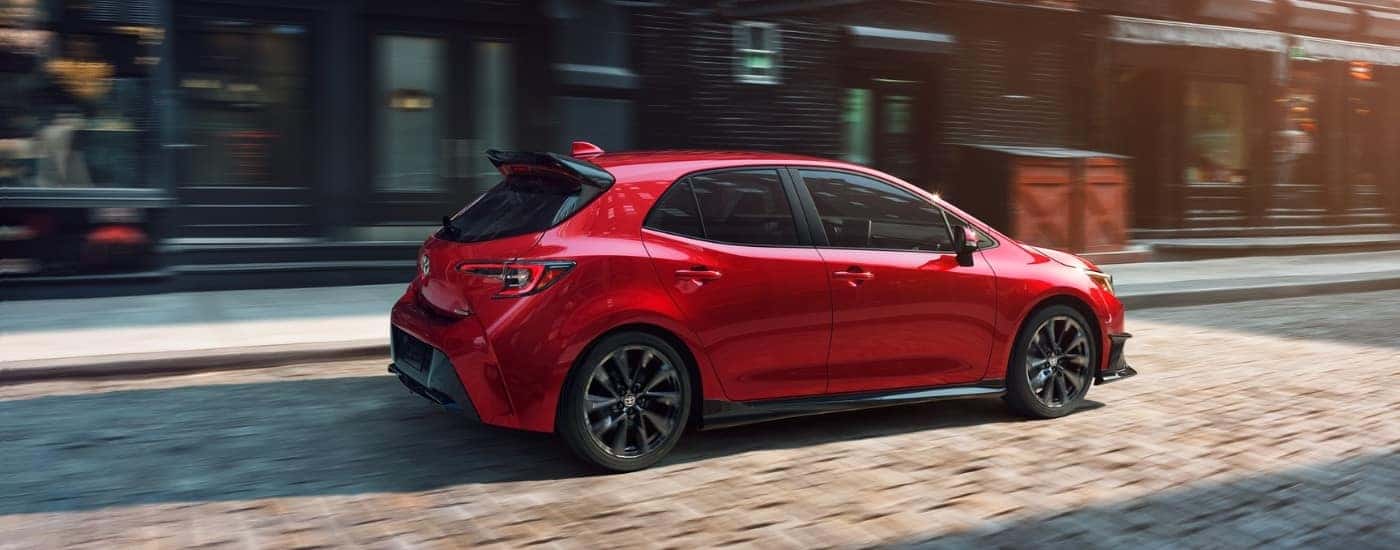 Red 2021 Toyota Corolla driving down a brick paved street