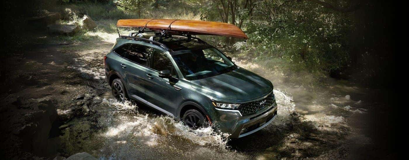 Green 2022 Kia Sorento X-Line with a canoe on top driving through a river