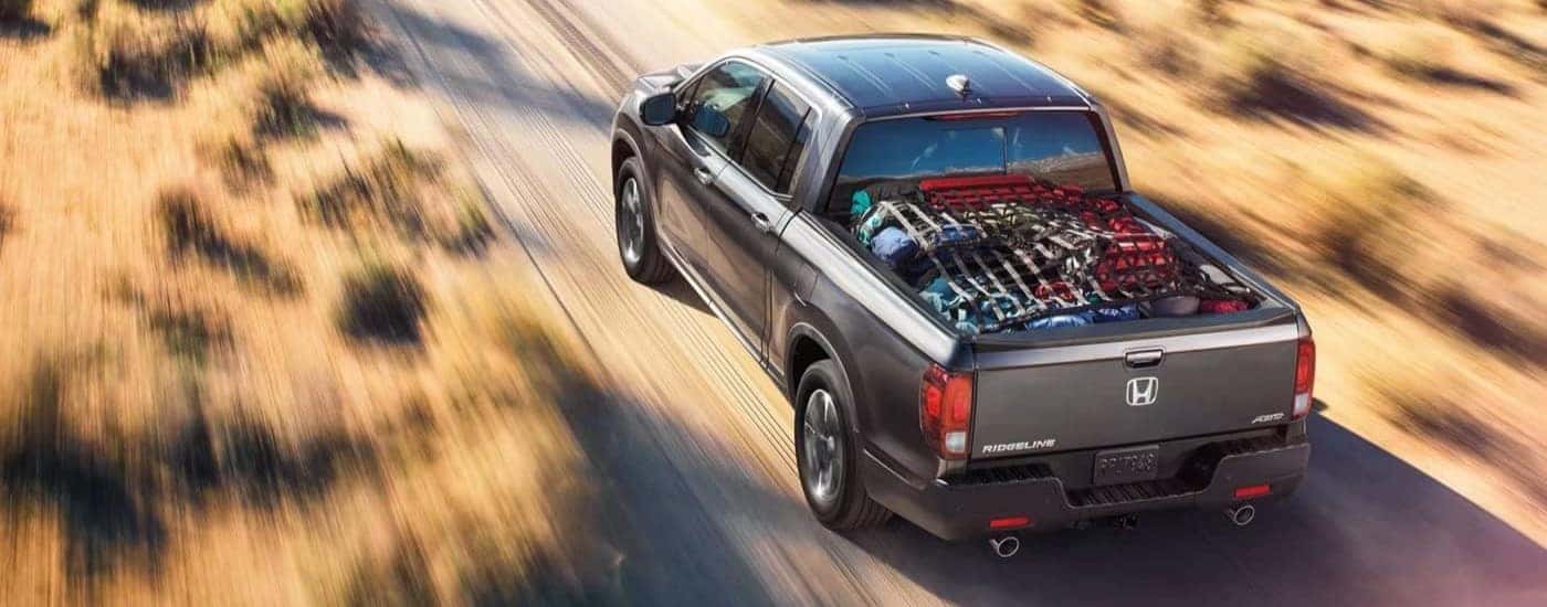 Grey 2023 Honda Ridgeline RTL-E with camping gear in the bed driving through a field.