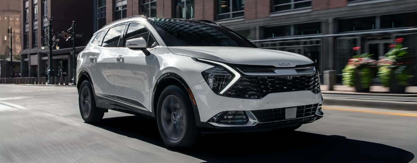 White 2023 Kia Sportage Hybrid driving down a city street