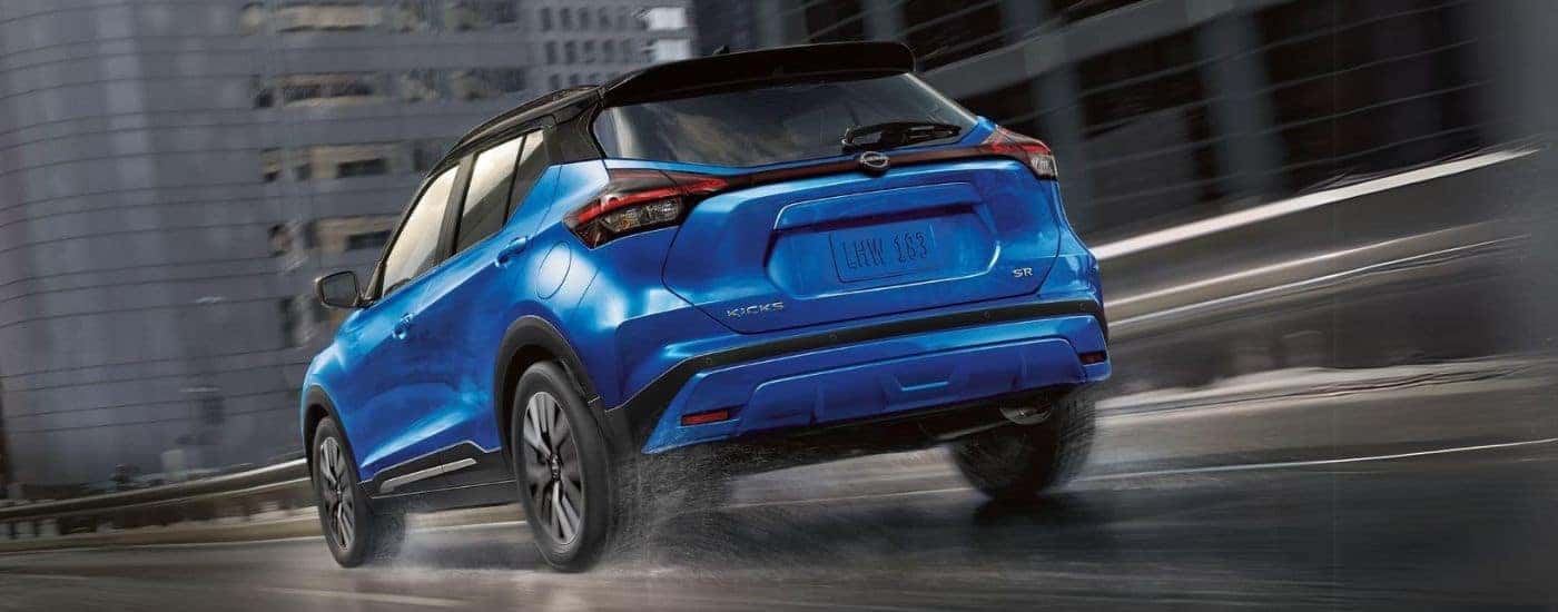 Rear view of a blue 2020 Nissan Kicks SR driving through a city from a used Nissan dealer.