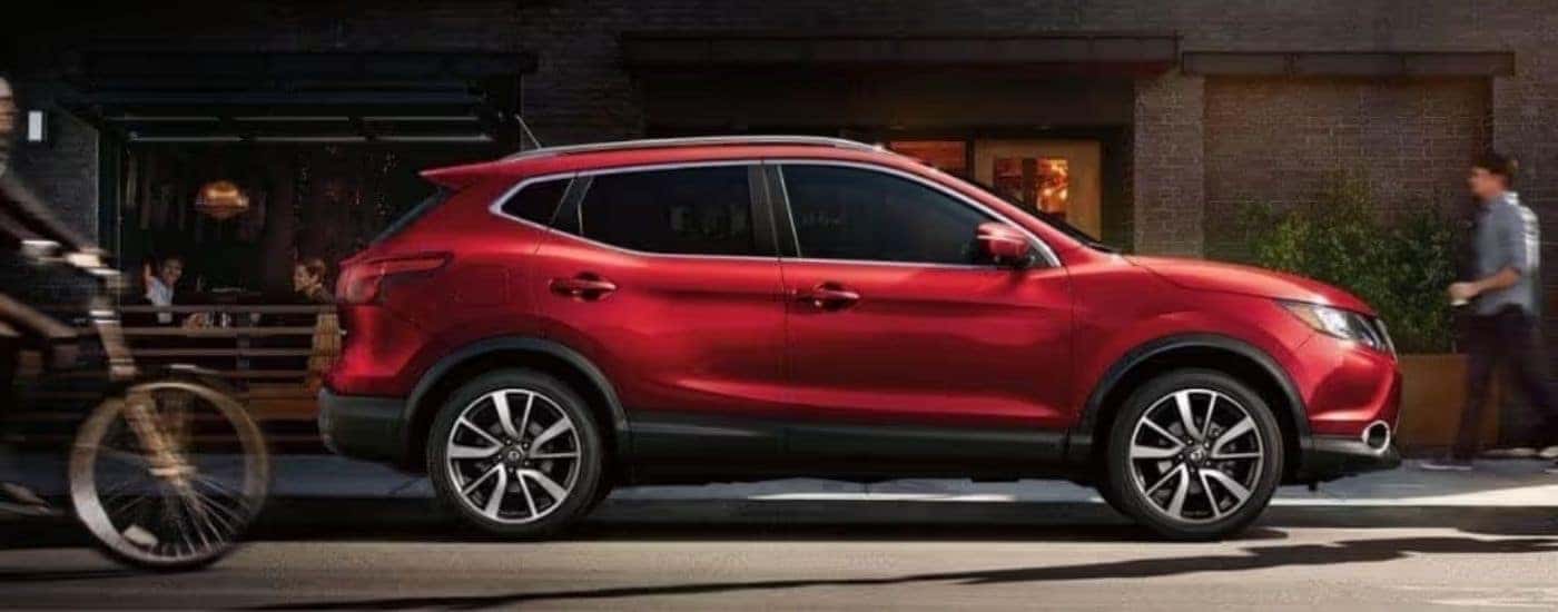 A red 2018 Nissan Rogue Sport is shown from the side parked on a city street.