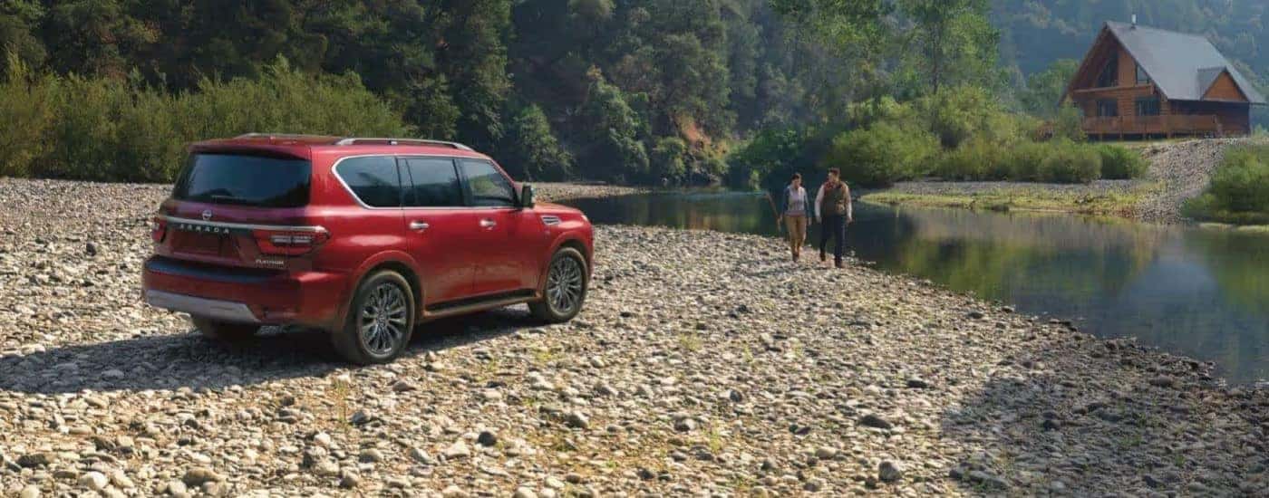 Rear view of a red 2023 Nissan Armada Platinum parked next to a cabin at a lake.