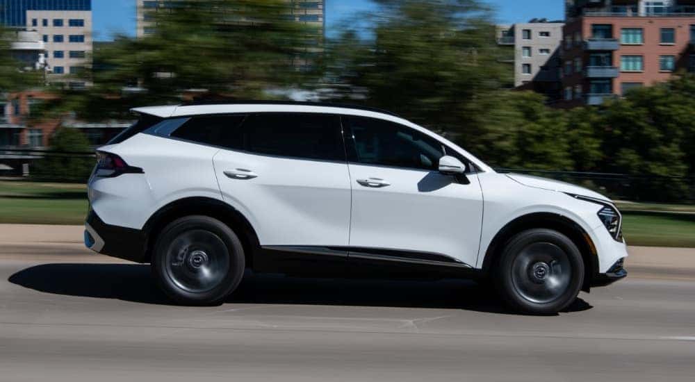 A white 2023 Kia Sportage Hybrid shown driving a city street from the side.